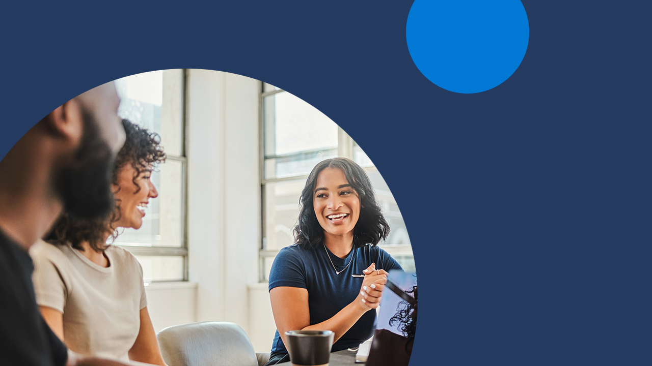A diverse group of coworkers collaborate in an office space while one takes notes on his laptop.
